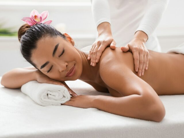 Relaxed Asian Woman Pampering Herself With Body Massage In Spa Salon